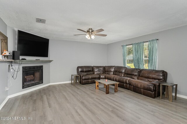 living room featuring ceiling fan, light wood-type flooring, and a textured ceiling