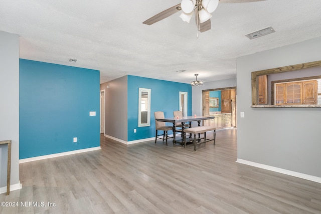 dining area featuring wood-type flooring, ceiling fan with notable chandelier, and a textured ceiling