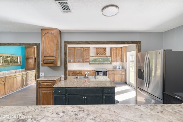 kitchen featuring sink, stainless steel appliances, light stone counters, light hardwood / wood-style flooring, and backsplash