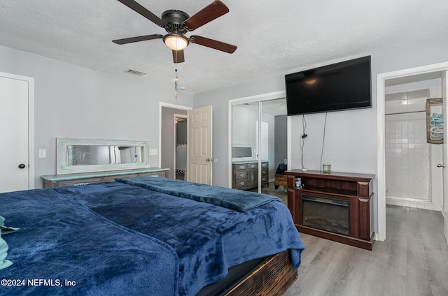 bedroom with ceiling fan, light hardwood / wood-style floors, a textured ceiling, and a closet