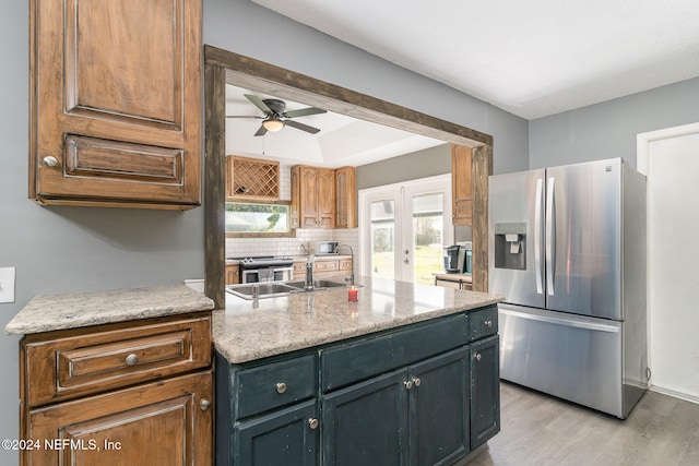 kitchen with light stone countertops, appliances with stainless steel finishes, ceiling fan, light hardwood / wood-style floors, and a kitchen island