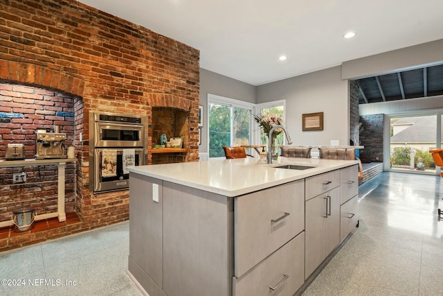 kitchen with stainless steel double oven, an island with sink, a wealth of natural light, and sink