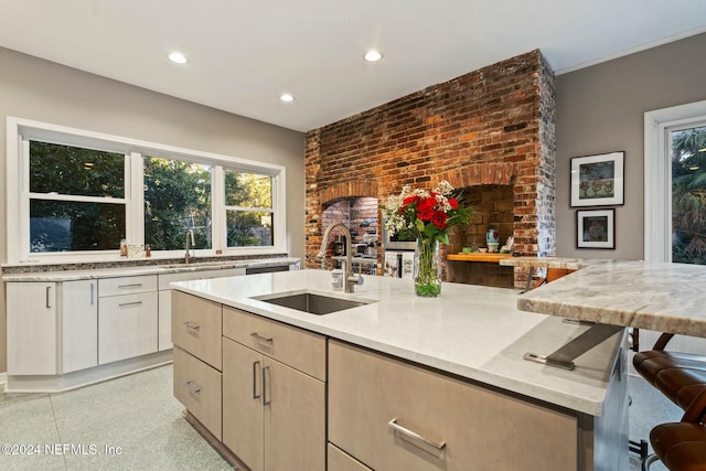 kitchen featuring a breakfast bar, sink, light brown cabinetry, light stone counters, and brick wall