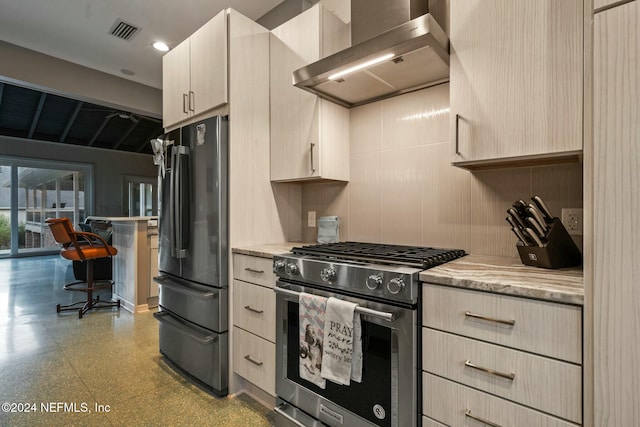 kitchen with light stone countertops, light brown cabinets, wall chimney range hood, and appliances with stainless steel finishes