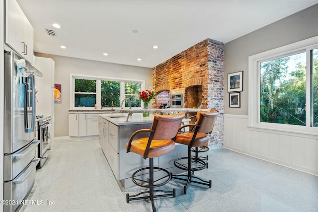 kitchen with an island with sink, plenty of natural light, white cabinets, and stainless steel appliances