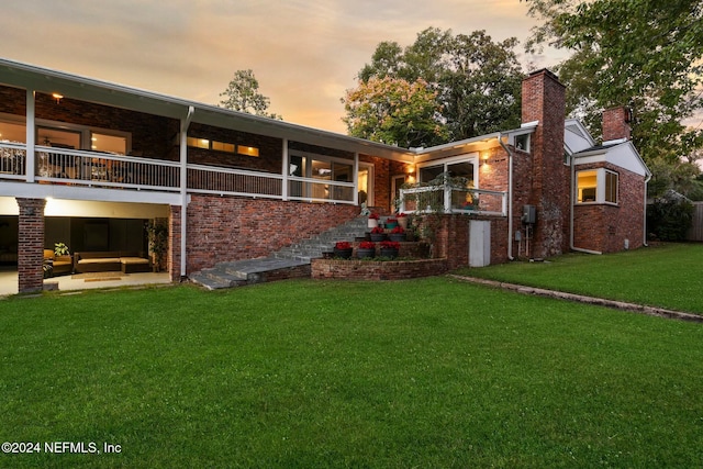 back house at dusk featuring a yard and a balcony