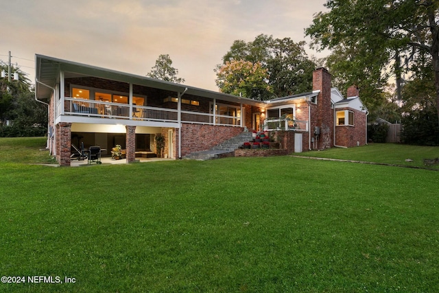 back house at dusk with a patio area, a yard, and a balcony