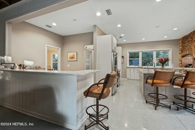 kitchen with a kitchen breakfast bar, stainless steel fridge, white cabinetry, and sink