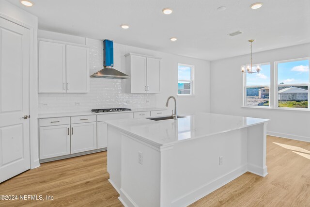 kitchen featuring plenty of natural light, a kitchen island with sink, and wall chimney range hood