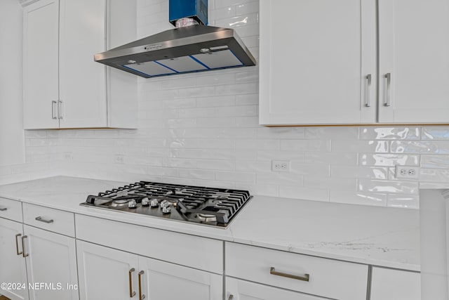 kitchen featuring white cabinets, stainless steel gas cooktop, backsplash, and exhaust hood