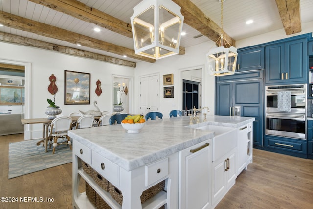 kitchen featuring white cabinetry, stainless steel double oven, blue cabinets, and a kitchen island with sink