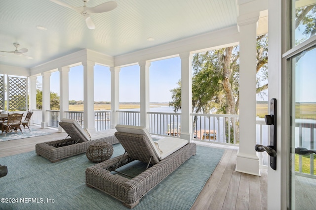 sunroom with ceiling fan and a water view