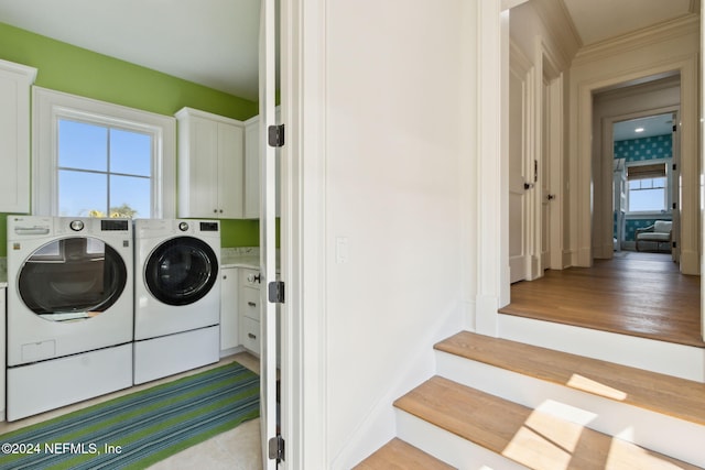 laundry area featuring independent washer and dryer, a wealth of natural light, cabinets, and light wood-type flooring