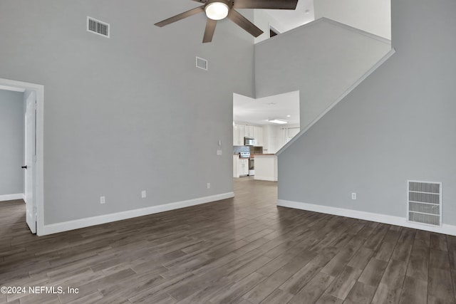 unfurnished living room featuring ceiling fan, dark hardwood / wood-style floors, and a towering ceiling