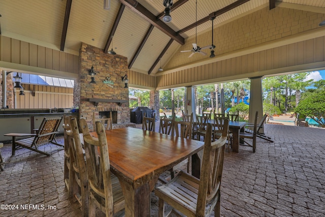 dining space with beamed ceiling, ceiling fan, an outdoor stone fireplace, and high vaulted ceiling