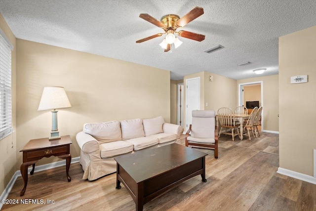 living room featuring ceiling fan, a textured ceiling, and light wood-type flooring