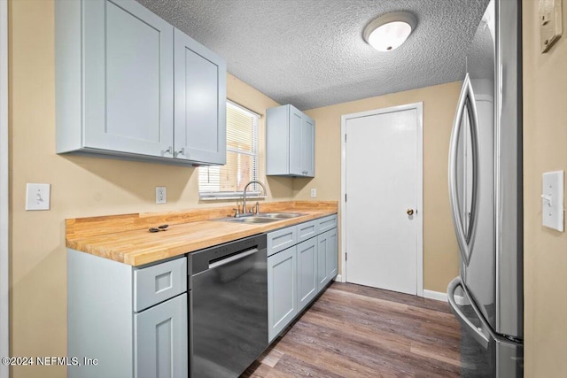 kitchen featuring wooden counters, sink, a textured ceiling, appliances with stainless steel finishes, and wood-type flooring