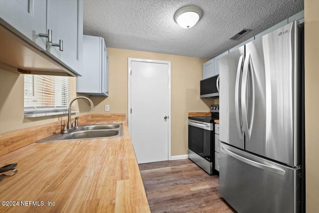 kitchen with dark wood-type flooring, white cabinets, sink, a textured ceiling, and stainless steel appliances