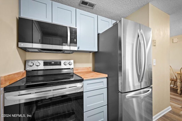 kitchen featuring appliances with stainless steel finishes, a textured ceiling, butcher block countertops, and hardwood / wood-style floors