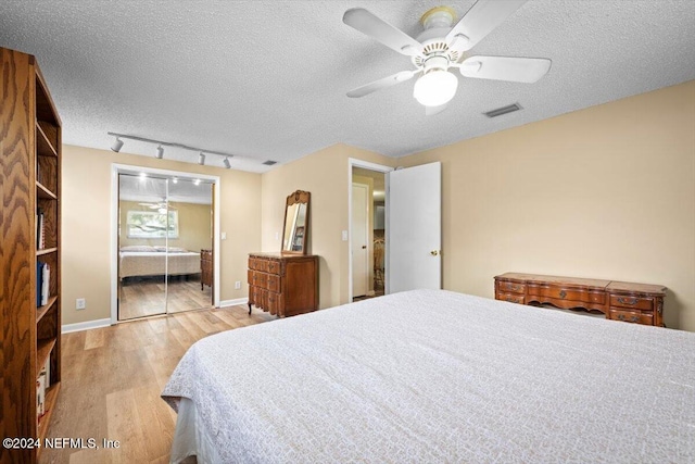 bedroom featuring rail lighting, ceiling fan, a textured ceiling, light hardwood / wood-style floors, and a closet