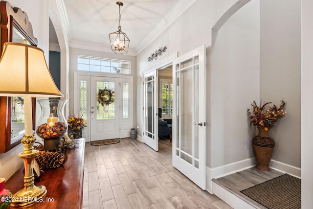 entrance foyer featuring a notable chandelier, light hardwood / wood-style floors, crown molding, and french doors