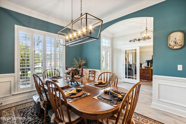 dining space with an inviting chandelier, light wood-type flooring, ornamental molding, and french doors