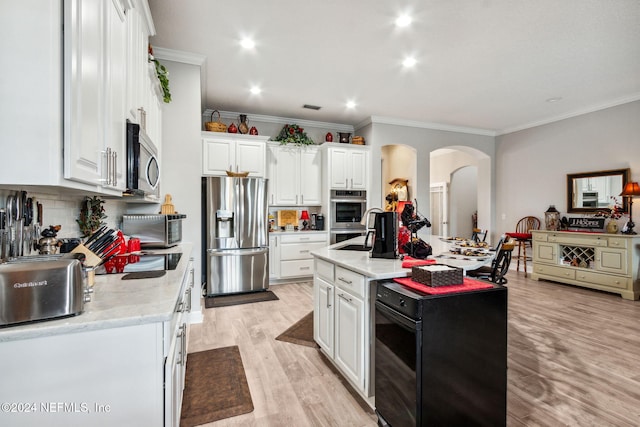 kitchen with light stone countertops, ornamental molding, appliances with stainless steel finishes, light hardwood / wood-style floors, and white cabinetry