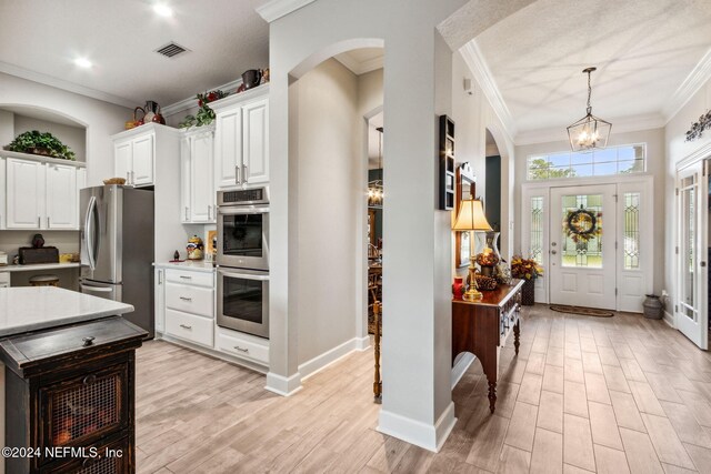 kitchen featuring stainless steel appliances, a notable chandelier, crown molding, light hardwood / wood-style floors, and white cabinets