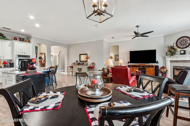 dining space featuring a fireplace, ceiling fan with notable chandelier, and ornamental molding