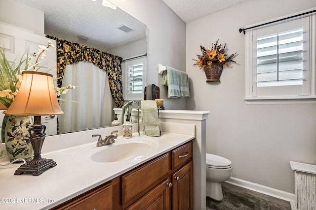 bathroom with a textured ceiling, vanity, toilet, and plenty of natural light