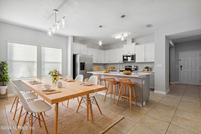 kitchen with white cabinetry, hanging light fixtures, an island with sink, and stainless steel appliances