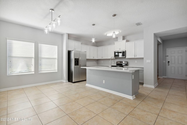 kitchen with appliances with stainless steel finishes, a kitchen island with sink, light tile patterned floors, decorative light fixtures, and white cabinetry