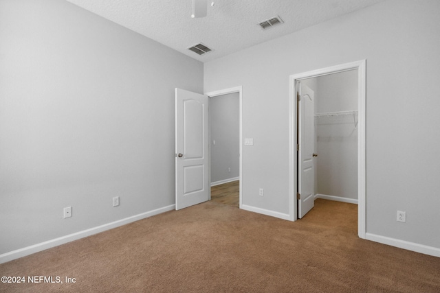 unfurnished bedroom with a walk in closet, a textured ceiling, ceiling fan, carpet floors, and a closet