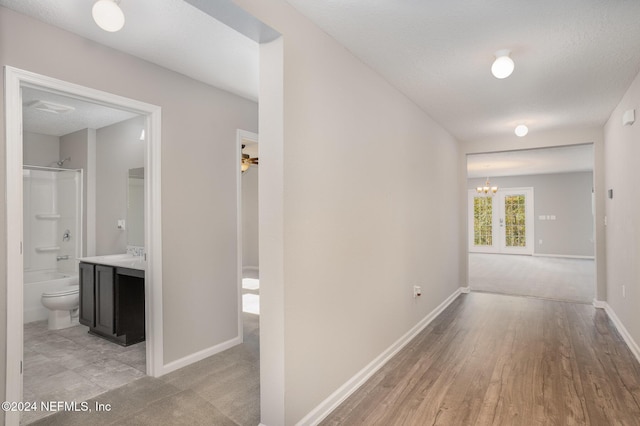 hall with a textured ceiling, a notable chandelier, light hardwood / wood-style floors, and sink