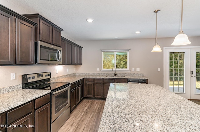 kitchen with sink, hanging light fixtures, light stone countertops, light wood-type flooring, and stainless steel appliances