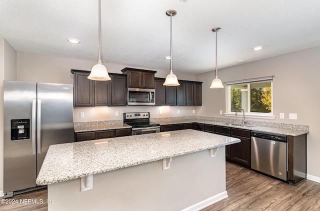 kitchen featuring pendant lighting, a center island, sink, appliances with stainless steel finishes, and wood-type flooring