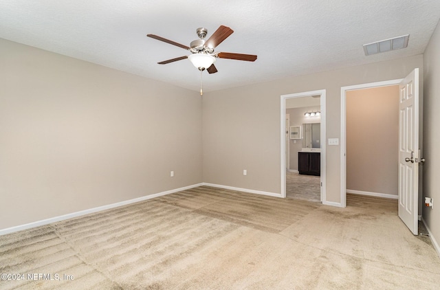 unfurnished bedroom with a textured ceiling, ceiling fan, light carpet, and connected bathroom