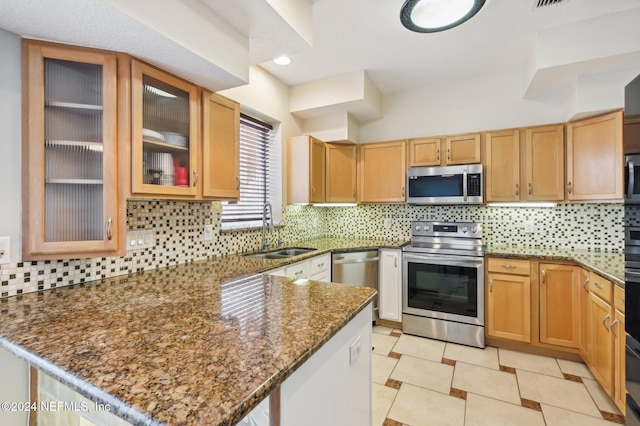 kitchen featuring backsplash, dark stone counters, sink, light tile patterned floors, and stainless steel appliances