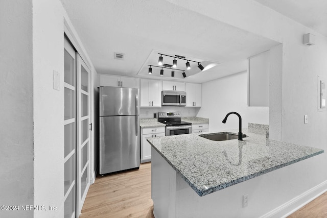 kitchen with kitchen peninsula, appliances with stainless steel finishes, light wood-type flooring, and white cabinetry