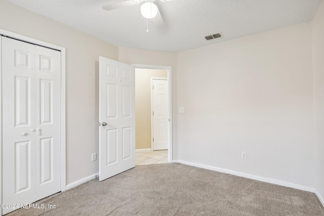 unfurnished bedroom with ceiling fan, a closet, light carpet, and a textured ceiling