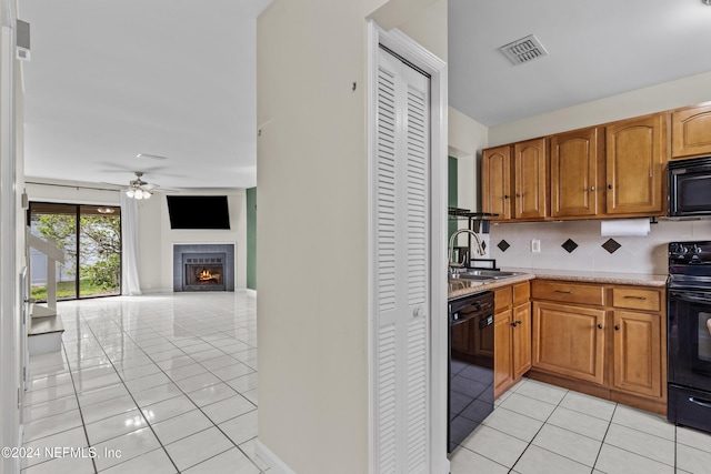 kitchen with decorative backsplash, sink, a tile fireplace, light tile patterned floors, and black appliances