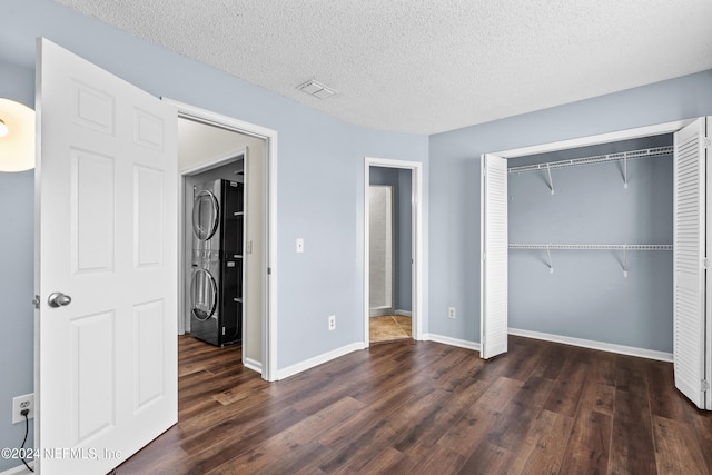 unfurnished bedroom with a textured ceiling, a closet, dark hardwood / wood-style floors, and stacked washer and clothes dryer