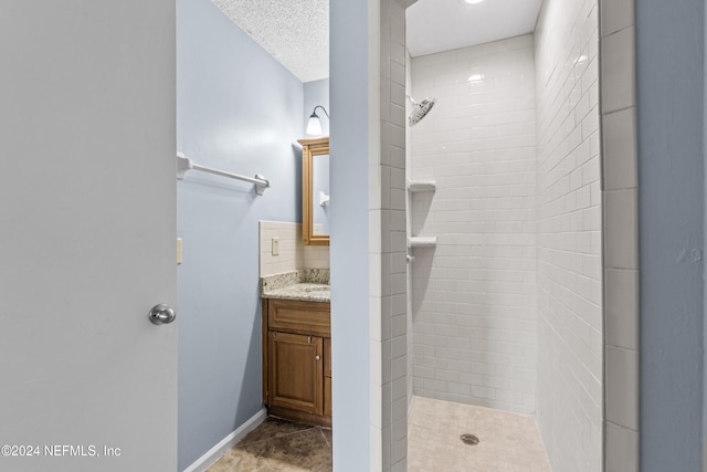 bathroom with tiled shower, a textured ceiling, and vanity