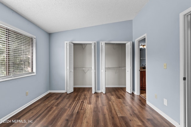 unfurnished bedroom featuring a textured ceiling, two closets, dark wood-type flooring, and lofted ceiling