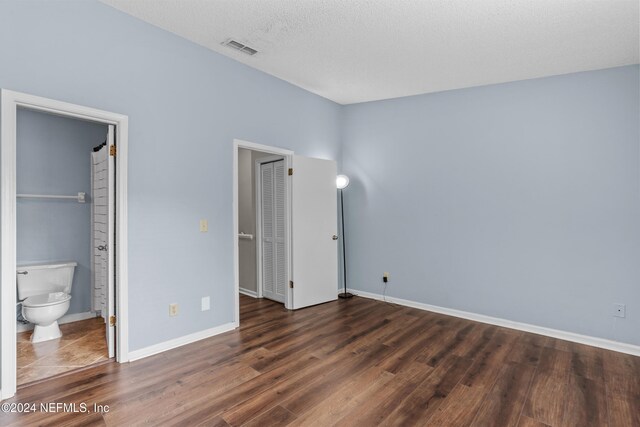 unfurnished bedroom featuring a textured ceiling, connected bathroom, and dark wood-type flooring