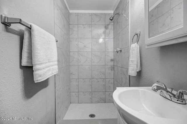 bathroom with tiled shower, sink, and ornamental molding