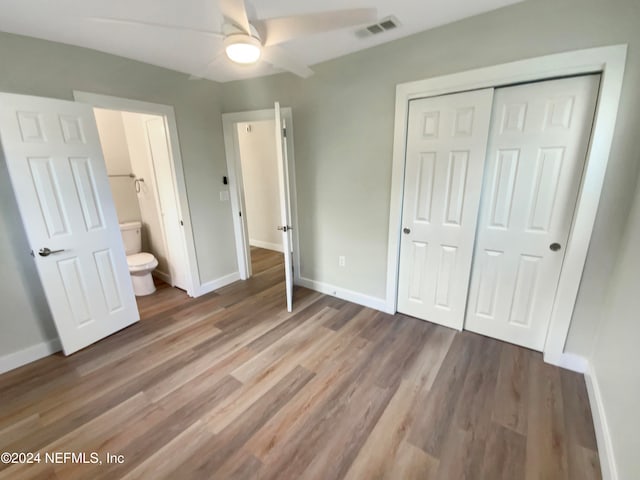 unfurnished bedroom with ensuite bath, ceiling fan, a closet, and hardwood / wood-style flooring