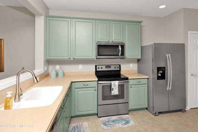 kitchen with light tile patterned flooring, stainless steel appliances, green cabinets, and sink