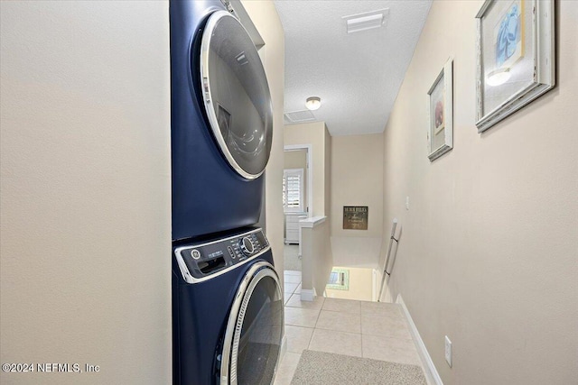 laundry room with a textured ceiling, light tile patterned floors, and stacked washer / dryer