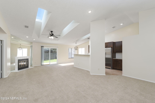 unfurnished living room with ceiling fan with notable chandelier, light colored carpet, a fireplace, and vaulted ceiling